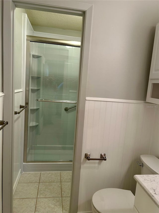 bathroom featuring a shower with shower door, toilet, vanity, and tile patterned flooring