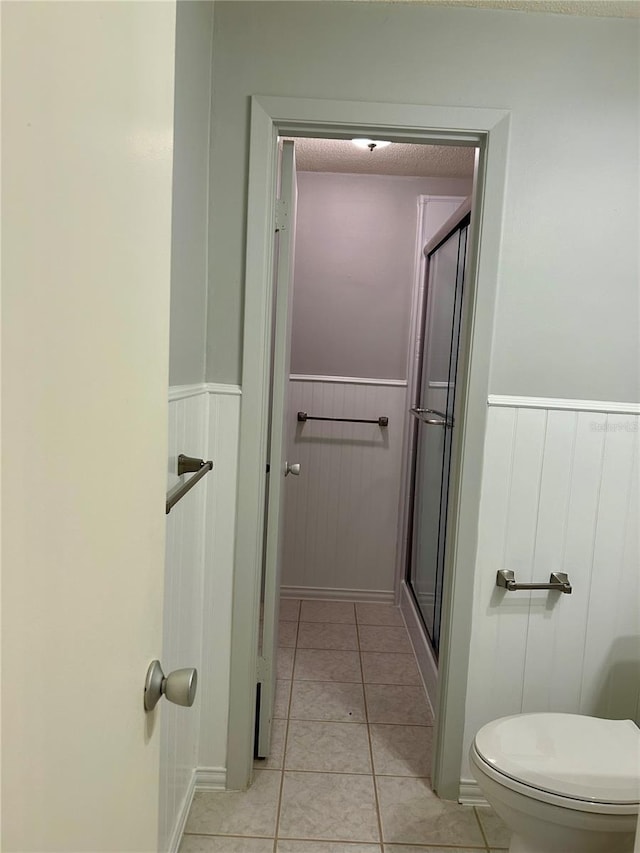 bathroom with toilet, tile patterned flooring, and a shower with shower door