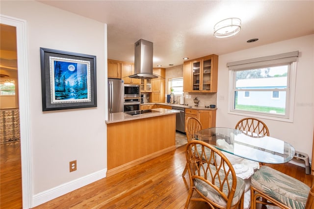 kitchen with backsplash, light hardwood / wood-style floors, stainless steel appliances, light stone counters, and island range hood