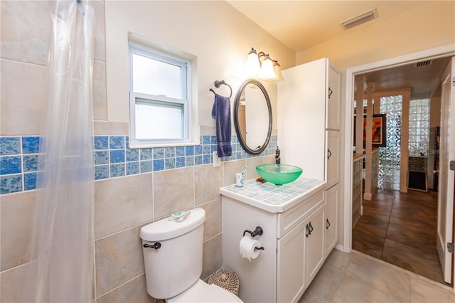 bathroom with toilet, vanity, a wealth of natural light, tile walls, and tile floors