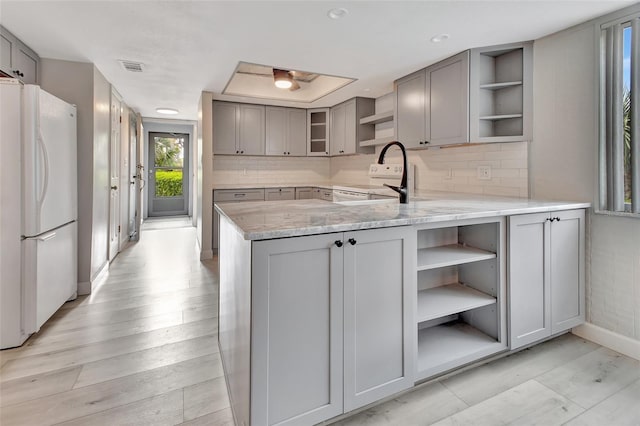 kitchen featuring light stone counters, open shelves, backsplash, gray cabinetry, and white appliances