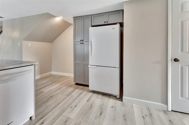 kitchen with lofted ceiling, light wood-style flooring, gray cabinetry, white appliances, and baseboards