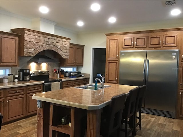 kitchen with a kitchen island with sink, sink, crown molding, stainless steel appliances, and dark wood-type flooring