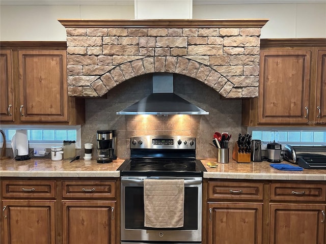 kitchen featuring backsplash, stainless steel range with electric cooktop, and wall chimney range hood