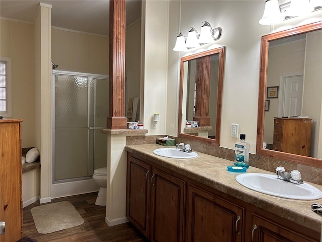 bathroom with toilet, double sink vanity, crown molding, a shower with door, and wood-type flooring