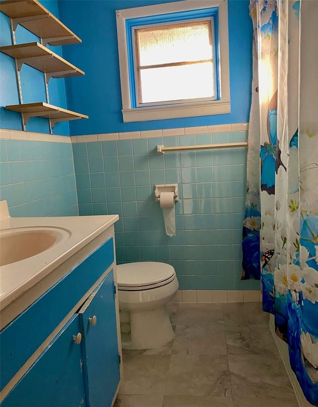 bathroom with walk in shower, vanity, tile walls, and toilet