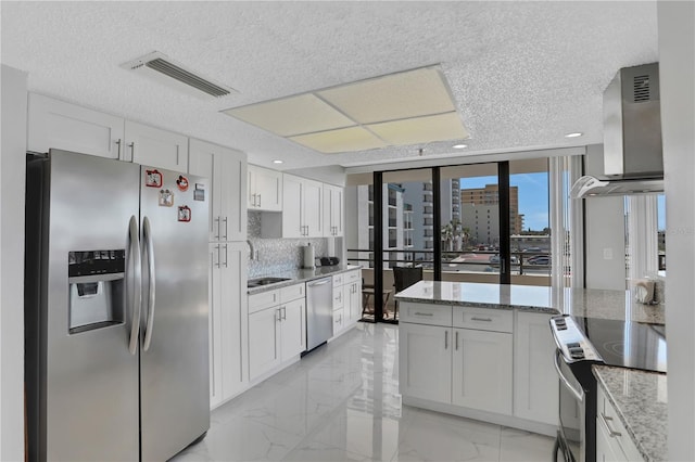 kitchen featuring appliances with stainless steel finishes, white cabinetry, and wall chimney range hood