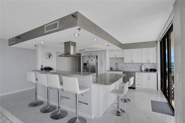 kitchen featuring white cabinetry, backsplash, appliances with stainless steel finishes, a breakfast bar, and dark stone counters