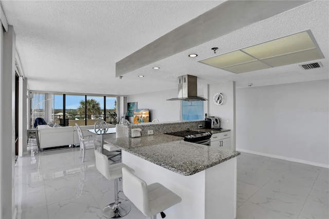 kitchen featuring light tile floors, dark stone counters, a breakfast bar, stainless steel electric range, and wall chimney exhaust hood