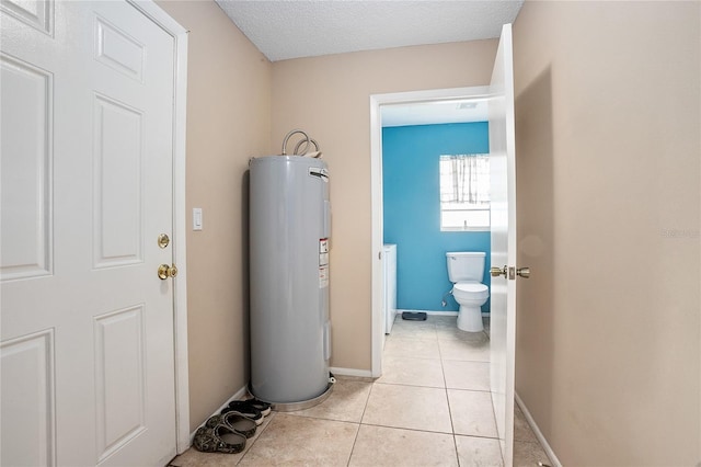 hall featuring a textured ceiling, electric water heater, and light tile floors