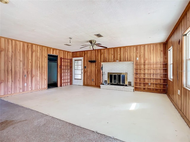 unfurnished living room with ceiling fan, a brick fireplace, and wooden walls