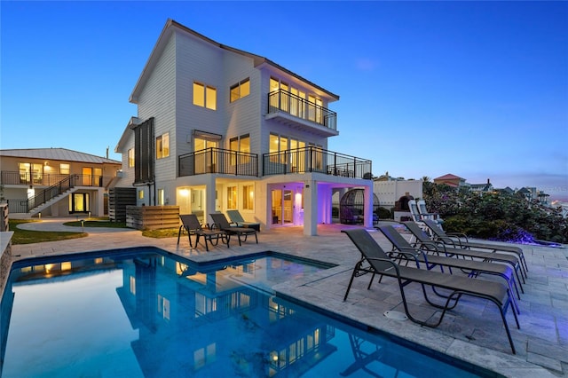 back house at dusk featuring a balcony and a patio area