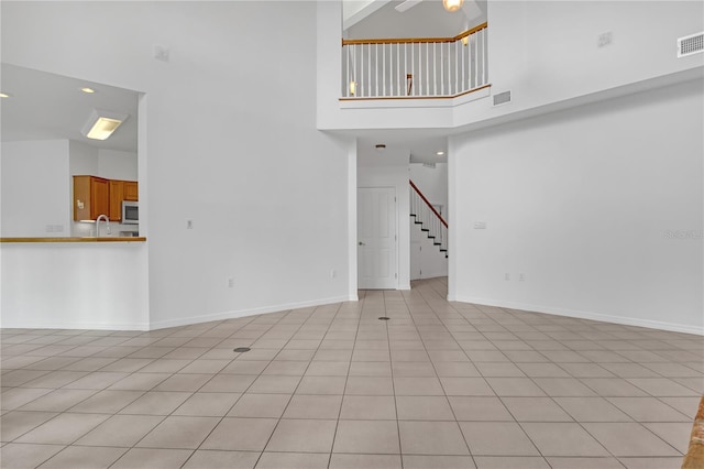 unfurnished living room featuring light tile patterned floors, sink, and a high ceiling