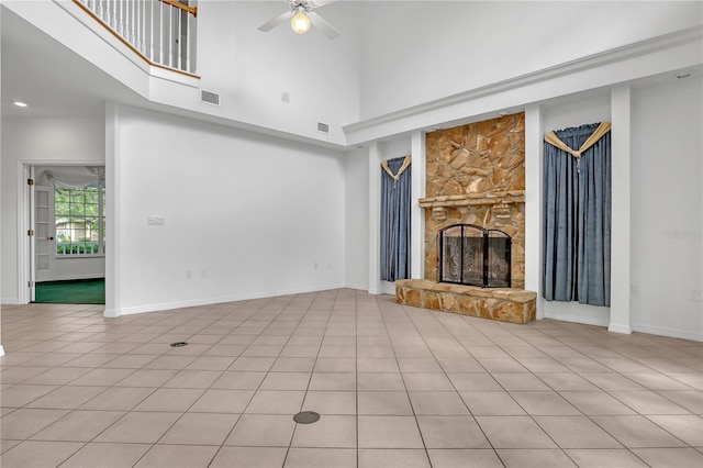 unfurnished living room featuring a high ceiling, a stone fireplace, light tile patterned floors, and ceiling fan