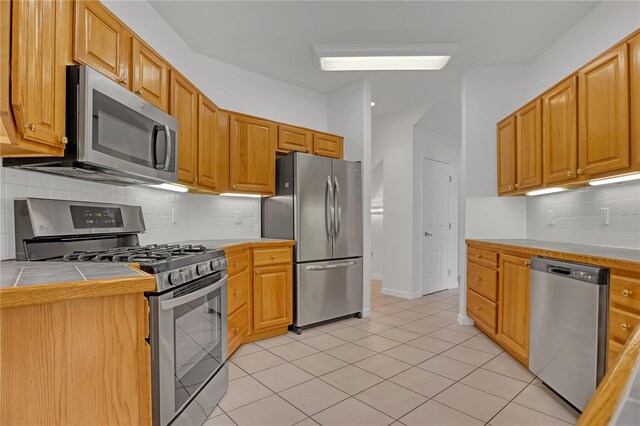 kitchen with tile counters, appliances with stainless steel finishes, light tile patterned floors, and backsplash