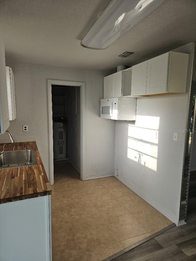 kitchen with light tile floors, white cabinetry, sink, and butcher block counters