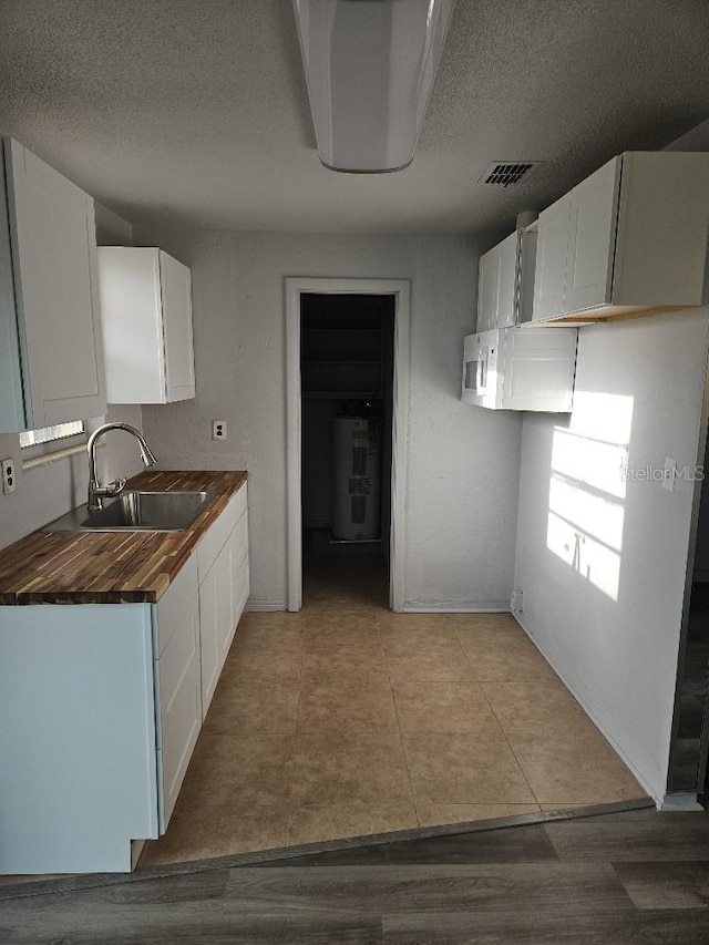 kitchen featuring light tile floors, white cabinets, wood counters, and sink