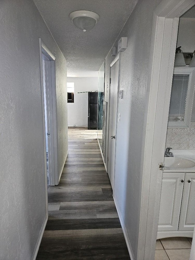 hallway with a textured ceiling, dark wood-type flooring, and sink