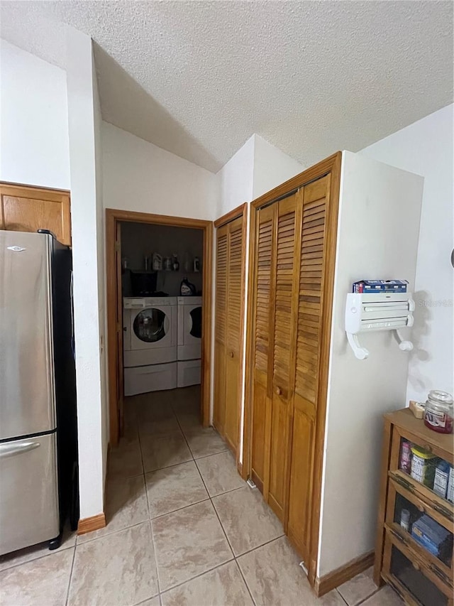 corridor with washer and clothes dryer, light tile patterned flooring, a textured ceiling, and vaulted ceiling