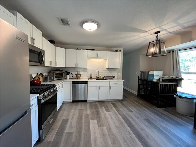 kitchen with sink, appliances with stainless steel finishes, decorative backsplash, white cabinets, and decorative light fixtures