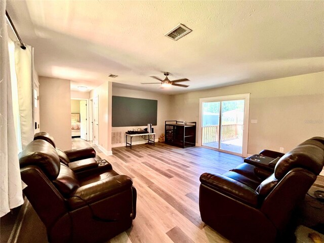 living room with ceiling fan, a textured ceiling, and light wood-type flooring