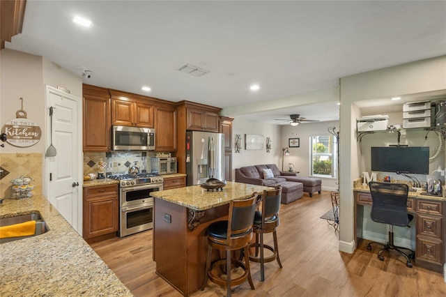 kitchen featuring backsplash, appliances with stainless steel finishes, a kitchen bar, light wood-type flooring, and ceiling fan