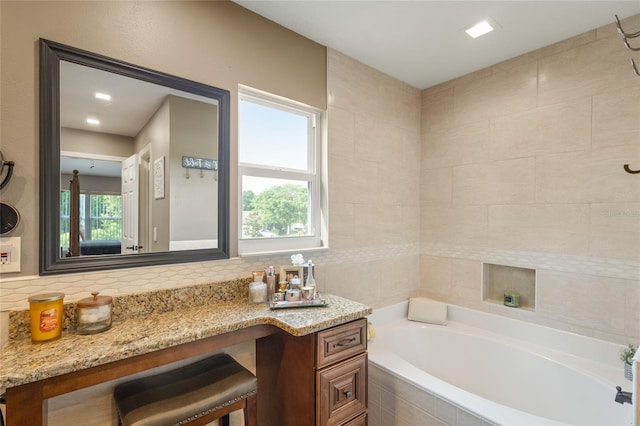 bathroom with tile walls, a relaxing tiled bath, tasteful backsplash, and vanity