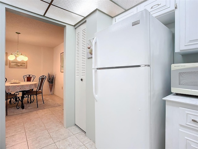 kitchen with decorative light fixtures, white appliances, white cabinetry, a chandelier, and light tile floors