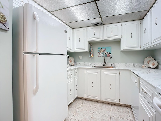 kitchen with a drop ceiling, white appliances, white cabinets, sink, and light tile floors