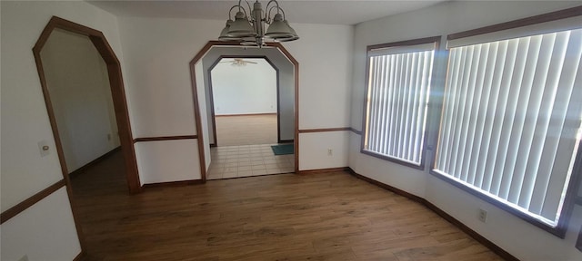 spare room featuring a wealth of natural light, wood-type flooring, and a notable chandelier