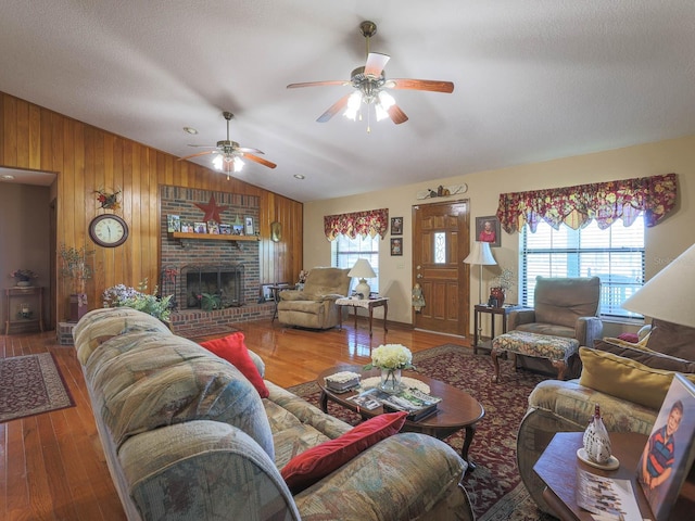 living room with wood walls, a brick fireplace, hardwood / wood-style floors, vaulted ceiling, and ceiling fan