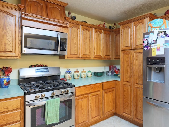 kitchen with appliances with stainless steel finishes, a textured ceiling, and light tile floors