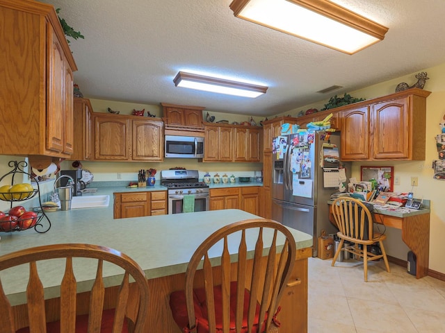 kitchen featuring appliances with stainless steel finishes, light tile floors, a textured ceiling, sink, and kitchen peninsula