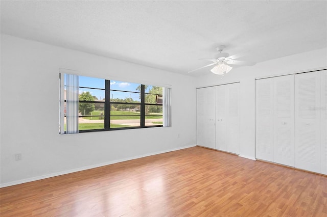 unfurnished bedroom with light hardwood / wood-style floors, ceiling fan, a textured ceiling, and multiple closets