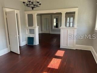 empty room with dark hardwood / wood-style flooring, ornate columns, and an inviting chandelier