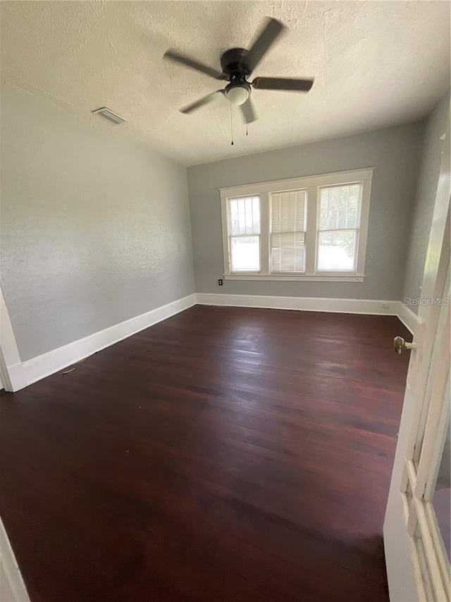 spare room featuring dark wood-type flooring, ceiling fan, and a textured ceiling