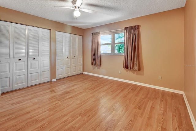 unfurnished bedroom with multiple closets, a textured ceiling, ceiling fan, and light wood-type flooring