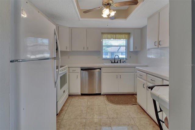 kitchen featuring sink, white appliances, white cabinets, and a raised ceiling