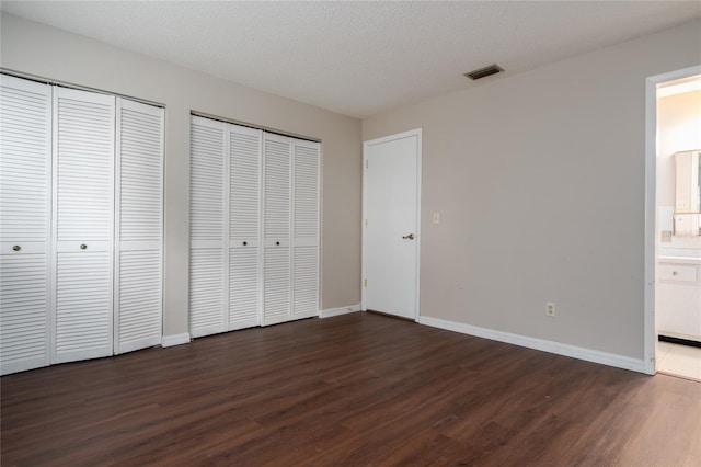 unfurnished bedroom with a textured ceiling, multiple closets, ensuite bathroom, and dark hardwood / wood-style floors