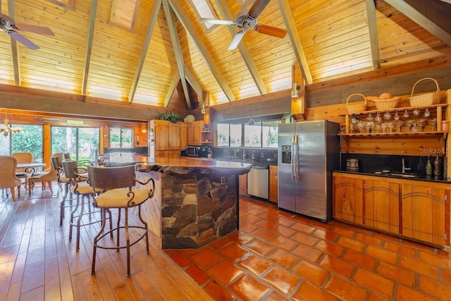 kitchen with ceiling fan with notable chandelier, stainless steel appliances, beam ceiling, hardwood / wood-style flooring, and high vaulted ceiling