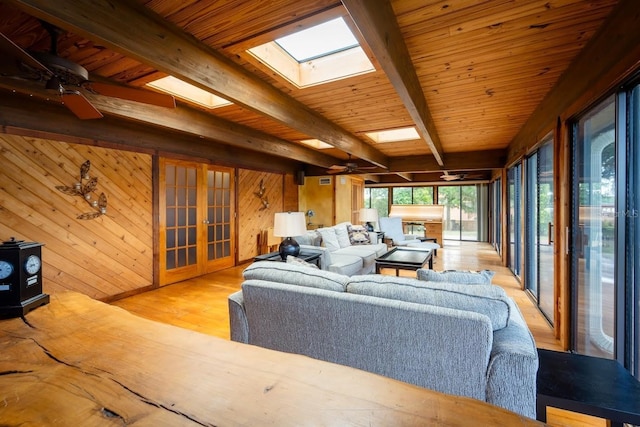 living room with wooden walls, light hardwood / wood-style flooring, a skylight, ceiling fan, and beam ceiling