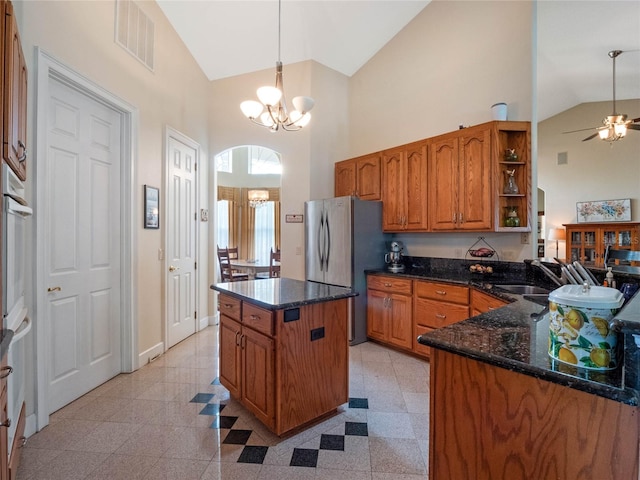 kitchen featuring decorative light fixtures, dark stone counters, ceiling fan with notable chandelier, high vaulted ceiling, and light tile floors