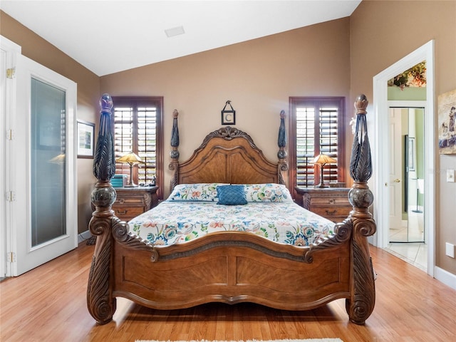 bedroom featuring multiple windows, ensuite bath, light hardwood / wood-style floors, and lofted ceiling