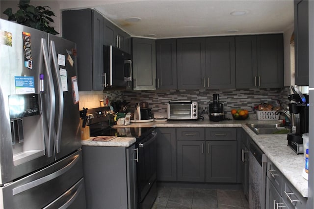 kitchen with appliances with stainless steel finishes, gray cabinets, backsplash, sink, and dark tile floors