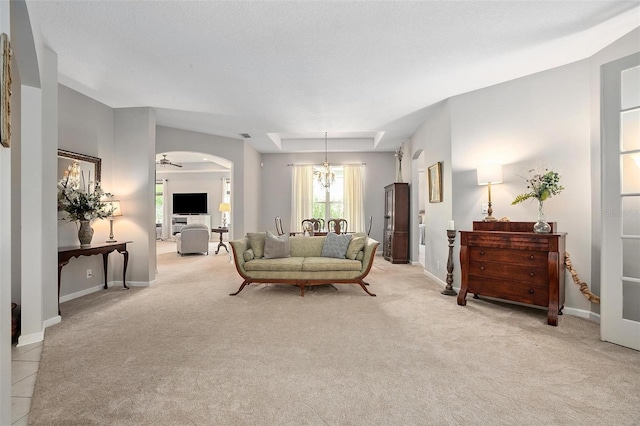 carpeted living room featuring a tray ceiling and ceiling fan with notable chandelier