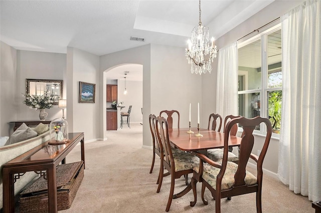 dining space with a notable chandelier, light carpet, and a raised ceiling