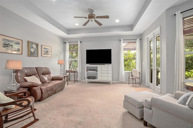 living room with a tray ceiling, a textured ceiling, ceiling fan, and light colored carpet