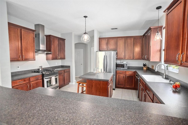 kitchen featuring light tile flooring, hanging light fixtures, a center island, wall chimney exhaust hood, and appliances with stainless steel finishes