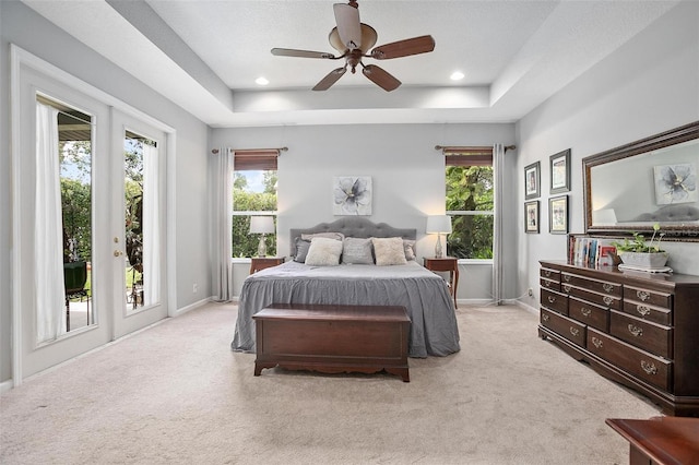 bedroom featuring a raised ceiling, ceiling fan, multiple windows, and light carpet