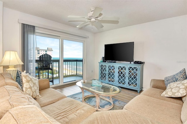 living room featuring ceiling fan, a textured ceiling, hardwood / wood-style flooring, and a water view